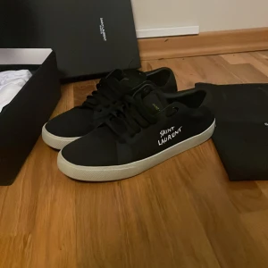 Svarta Saint Laurent sneakers - Svarta sneakers från Saint Laurent med vit sula och handskriven logga på sidan. Mycket bra skick knappt använda. Storlek 43 men passar 42.