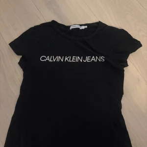 Svart Calvin Klein Jeans t-shirt XS - Svart t-shirt från Calvin Klein Jeans i storlek XS. Klassisk modell med rund halsringning och vit logotyptext framtill. T-shirten är i mjuk bomull och har korta ärmar. Perfekt för en clean och stilren look.
