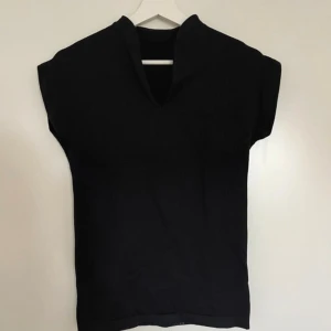Svart ribbad topp från New Apparel - Svart ribbad träningstopp från New Apparel i storlek S. Modellen är ärmlös med v-ringad hals. Materialet är mjukt och stretchigt. Passar dig som vill ha en enkel men snygg topp till träning eller vardags. 