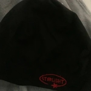 Svart mössa Starlight med röd logga - Svart mössa från Starlight med röd broderad logga och stjärna framtill. Enkel och stilren design, mjukt material som sitter skönt på huvudet. Perfekt för dig som gillar streetstyle och vill ha en clean look.