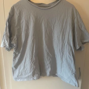 Ljusgrå t-shirt från 157 i XL - En enkel och stilren ljusgrå t-shirt från 157 i storlek XL. T-shirten har rund hals och korta ärmar, tillverkad i mjuk 100% bomull. Perfekt för dig som gillar en clean och avslappnad look.