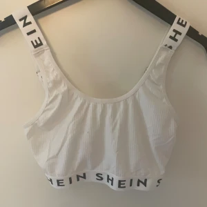 Vit ribbad linnetopp från SHEIN - Säljer en vit ribbad linnetopp från SHEIN med breda axelband och resår med logga både under bysten och på banden. Toppen är ärmlös och har justerbara axelband för bästa passform. Materialet är en mix av bomull och polyester.