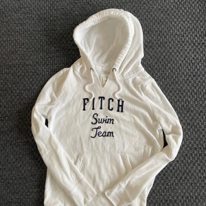 Sällsynt vintage Abercrombie & Fitch Hoodie  - Vit hoodie från Abercrombie & Fitch med broderad text 'Fitch Swim Team' i mörkblått på bröstet. Tröjan har huva med snörning, känguruficka och långa ärmar. Mjuk bomullskvalitet som är skön att ha på sig. Perfekt för chill dagar. Riktigt fint skick och ett eftertraktat och unikt tryck😁 Skriv vid funderingar 🙌