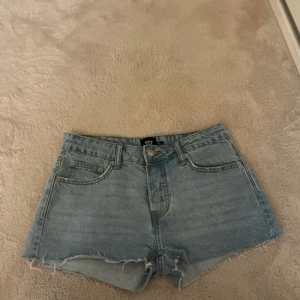 Ljusblå denimshorts från 157 - Snygga ljusblå denimshorts från 157 med råa kanter och klassisk femficksmodell. Låg midja och avslappnad passform, perfekta för sommardagar. Gjorda i bomull för en skön känsla. Styla med en crop top eller hoodie för en chill look. Helt oanvända men har tyvärr dragit bort prislappen 