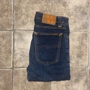 Nudie Jeans  - Mörkblå skinny jeans från Nudie Jeans, modell High Kai. Hög midja och klassisk femficksdesign med orangea sömmar och läderpatch bak. Tillverkade i stretchig bomullsdenim för en tight passform. Midja 32cm, längd 99cm. Ifall det inte finns någon bild i annonsen där jag bär plaggen jag säljer så är det för att jag ej kan ha storleken heller passformen, så kolla måtten för storlek och googla på modellnamnet för passform 😉 OBS jeansen är uppklippta, se sista bild. S4 
