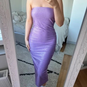Lila glittrig tubklänning Gina Tricot 💜 - Säljer en lila glittrig tubklänning från Gina Tricot i storlek XS. Klänningen är lång, figurnära och har en snygg slits bak. Materialet är stretchigt och skimrar i ljuset. Den är axelbandslös och har en slim passform som framhäver siluetten. Fint skick 💜