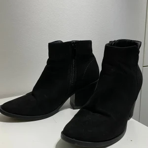 Svarta mocka stövletter från Alley - Snygga svarta stövletter från Alley i storlek 37. Skorna har en spetsig tå, klack och är gjorda i mjuk mocka. Dragkedja på sidan gör dem enkla att ta på och av. Perfekta för dig som gillar stilrena boots med lite höjd.