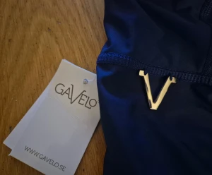 Blå leggings från Gavelo med ribbade detaljer - Ny med Prislappen kvar. Snygga blå leggings från Gavelo med coola ribbade detaljer över knäna och hög midja. Gjorda i stretchigt material av polyester och spandex för perfekt passform. Logga framtill och bak, samt elastisk midja för extra komfort.