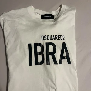 Vit DSQUARED2 IBRA t-shirt - Vit t-shirt från DSQUARED2 med svart tryck 'IBRA' på bröstet. Klassisk rund hals och korta ärmar. Skön och mjuk i bomull, perfekt för dig som gillar stilrena statement-plagg och vill sticka ut med en ikonisk look.