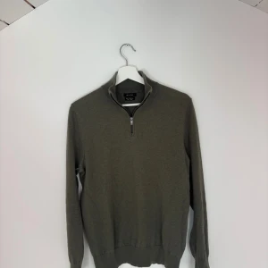 Olivgrön halvzip tröja Massimo Dutti  - Olivgrön långärmad tröja från Massimo Dutti med halv dragkedja vid kragen. Tröjan har en stilren design med ribbade muddar och är tillverkad i mjuk bomull. 