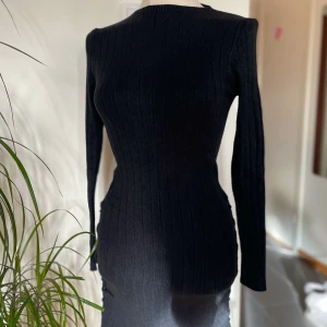 Svart ribbad långärmad klänning - Snygg svart ribbad klänning med lång ärm och figurnära passform. Klänningen har cool snörningsdetalj längs sidan som ger en unik touch. Materialet är stickat och känns mjukt mot huden. Perfekt för dig som gillar stilrena och moderna plagg.
