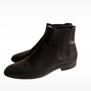 Saint Laurent Hedi Slimane Chelsea Boots - Snygga svarta chelsea boots från Saint Laurent Paris i slätt skinn. Klassisk siluett med rund tå, elastiska paneler på sidorna och låg klack. Perfekt för dig som gillar stilrena och tidlösa skor med lyxig känsla.
