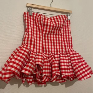 Rutig röd strapless topp från NA-KD - Superfin rutig topp från NA-KD i rött och vitt. Strapless modell med volang nedtill. Toppen har en figurnära passform upptill och en fluffig kjol. Köpt för lite mer än ett år sedan, endast använd 1 gång. 