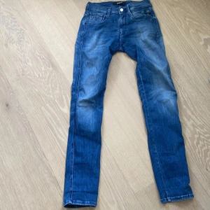 Blå Replay Anbass jeans - Säljer ett par blå Replay Anbass jeans med klassisk femficksdesign.. Jeansen har slim passfomr samt detaljer som dragkedja och knappar. Perfekta för dig som gillar stilrena och bekväma jeans.