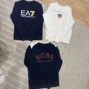 Tre snygga tröjor från EA7, GANT & Hugo Boss - PAKET PRIS FÖR ALLA 1100kr.✨🌟.               Säljer tre stilrena tröjor i marinblått och vitt från EA7 Emporio Armani, GANT och Hugo Boss. Alla har lång ärm och tryck på bröstet, GANT med emblem, EA7 med logga i vitt och gult, Hugo Boss med röd text och vit axeldetalj. Perfekt för dig som gillar märkeskläder.