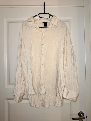 Oversized vit skjorta från Lindex - Luftig och oversized vit skjorta från Lindex i skrynklig bomull. Klassisk krage, knäppning framtill och långa ärmar med breda manschetter. Perfekt för en chill och avslappnad look.