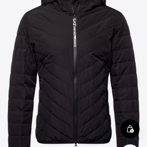 Svart pufferjacka från Emporio Armani - Svart pufferjacka från Emporio Armani med huva och snyggt mönstrad quiltning. Jackan har dragkedja framtill med logotyp, två sidofickor och lång ärm. Perfekt för dig som vill ha en stilren och modern look under höst och vinter.