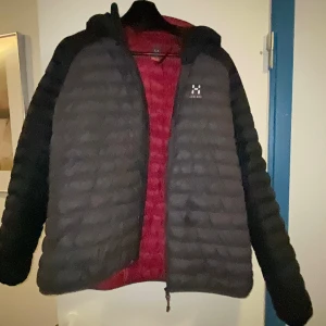 Svart dunjacka Haglöfs dam XL - Säljer en svart dunjacka från Haglöfs i dammodell, storlek XL. Jackan har quiltad design, huva och dragkedja framtill. Insidan är röd och materialet är syntet med dunfyllning. Perfekt för kalla dagar och outdoor vibes. Går till killar med 👍 