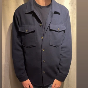 Mörkblå overshirt(strömberg) - Snygg mörkblå overshirt med klassisk krage och stora bröstfickor med knappar. Jackan har knappstängning framtill och långärmade ärmar. Perfekt för lager-på-lager och chill stil. Materialet känns mjukt och har en lite tjockare känsla.