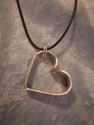 Handgjord halsband återbruk  - Egentillverkat halsband skapat av en sked gjord i nysilver. Hjärtat är ca 4cm brett och 3cm högt. Hänger i ett svart band som är justerbart. Blir en fin och stilren accessoar.