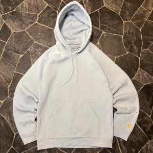 Carhartt Hoodie  - Snygg ljusgrå hoodie från Carhartt i storlek S. Tröjan har en klassisk huva med snörning, stor magficka och Carhartt-logga broderad i gult på ärmen. Tillverkad i mjuk bomull och har ribbade muddar vid ärmslut och nederkant. Perfekt för chill dagar.