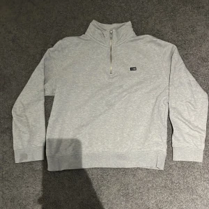 Grå half zip tröja från Lexington Barn - Snygg ljusgrå långärmad tröja från Lexington med half zip och liten logotyp på bröstet. Tröjan har en hög krage och är gjord i mjuk bomull, perfekt för chill dagar. Passformen är normal och materialet känns riktigt skönt mot huden.