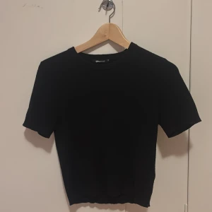 Svart stickad topp från Gina Tricot - Svart, croppad stickad topp från Gina Tricot i storlek XS. Lite nopprig.Modellen har rund hals och korta ärmar, perfekt för dig som gillar enkel och stilren look. Mjuk stickad känsla och snygg passform som sitter lite tight. Enkelt att matcha med dina favoritjeans eller kjol. 