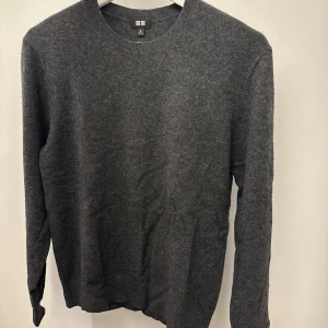 Mörkgrå kashmirtröja från Uniqlo XS - Snygg mörkgrå rundhalsad tröja från Uniqlo i 100% kashmir. Tröjan har en klassisk, enkel design med lång ärm och ribbade muddar vid hals, ärmslut och nederkant. Perfekt för dig som gillar stilrena och mjuka plagg. Nypris 1299! 