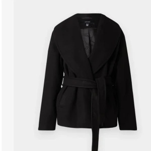 Svart kappa Vero Moda - Stilren svart jacka från Vero Moda med bred krag och knytbälte i midjan. Jackan har omlottmodell och är tillverkad i ett mjukt ullblandat material. Perfekt för dig som gillar en clean look med lite extra edge. Skriv privat för fler bilder