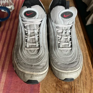 Nike Air Max 97 Silver Bullet 45 - Nike Air Max 97 Silver Bullet i storlek 45. Ikoniska sneakers med vågformad design, silvriga paneler och röda Swoosh-detaljer. Ovandel i mesh och syntet, svart yttersula och synlig Air-enhet. Klassisk snörning och reflekterande detaljer för extra stil.