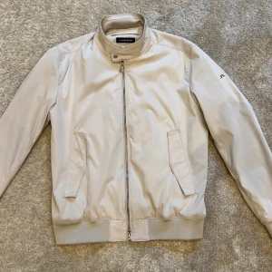 Beige Vår/Höst jacka från J.Lindeberg - Stilig beige jack ifrån J.Lindeberg. Använd 2 gånger och är i exptremt bra skick, storlek XL. Jackan köptes i butik nypris ca 2500kr. Ställ gärna frågor om varan, bilder osv.. Kvitto medföljer tyvär ej.