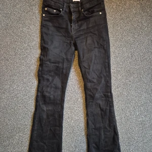 Svarta bootcut jeans från Grunt  - Svarta low waist jeans från Grunt i klassisk bootcut-modell. Snyggt svarta med fem fickor och knappstängning framtill. Jeansen är tillverkade i ett mjukt bomullstyg med lite stretch för extra komfort. Perfekta för dig som gillar en tidlös och clean look.
