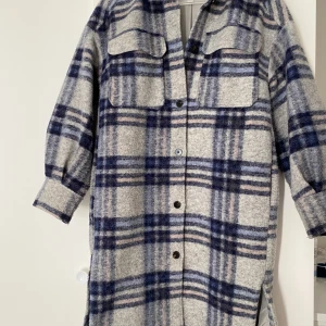 Rutig overshirt från H&M i ullmix XS - Overshirt från H&M i storlek XS med grå och blå rutor. Jackan har två stora bröstfickor med lock, knappar framtill och nedhasade axlar. Materialet är en ullmix som ger en mysig och trendig känsla. Perfekt för lager-på-lager-stil.