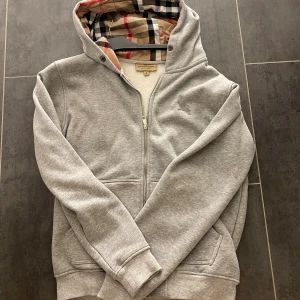 Grå burberry hoodie - Tjena, Säljer en grå burberry hoodie som är perfekt till vintern/hösten som kommer. Tjockt material och snygg hoodie. Aldrig använd och är helt ny. Säljer för bra pris och fraktas samma dag. Skriv vid intresse. Kan gå ner vid snabb affär☺️