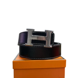 Svart  skärp med H-spänne - Snyggt svart skärp från  med ett stort H-format spänne i silverfärgad metall. Bältet är gjort av skinn med vit kontrastsöm längs kanterna och har en klassisk, stilren design som lyfter vilken outfit som helst.
