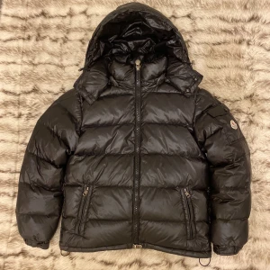 Svart Moncler pufferjacka med huva - Säljer en svart pufferjacka från Moncler med huva och dragkedja framtill. Jackan har två fickor med dragkedja, snygg design och klassisk Moncler-logga på ärmen. NFC fungerar och sitter i Moncler-loggan. Den är köpt december 2024. Jag har kvittot online. Har kvar en hängetikett som kom med jackan. Priset kan diskuteras!