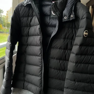 Svart dunjacka från Colmar - Säljer en svart dunjacka från Colmar med huva, jackan är storlek 50 vilket motsvarar M. Jackan är i nyskick utan några skavanker eller märken, använd 4-5 gånger. Har kvar tags och kvitto ifrån köpet. Pris kan diskuteras
