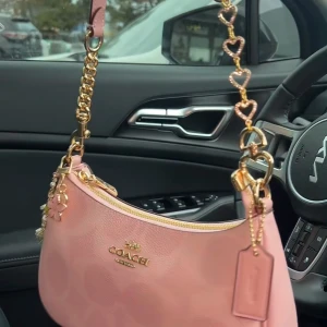 Rosa coach axelväska - Superfin rosa axelväska i skinn med guldfärgade detaljer. Väskan har dragkedja upptill. Perfekt accessoar för att lyfta din look med denna super fina väska!