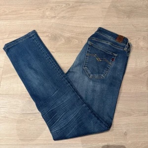 Blå Replay jeans  - Snygga blå jeans från Replay med klassisk bootcut och normal passform. Jeansen har fem fickor, ljusa slitningar och detaljerade bakfickor med gul söm. Tillverkade i mjukt jeanstyg som sitter skönt hela dagen. Fickorna är dock lite små