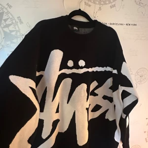 Svartvit stickad Stüssy tröja - Säljer en svart och vit stickad tröja från Stüssy med stor grafisk logga över hela framsidan. Tröjan är oversized men med storleken Large 