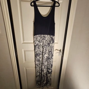 Marinblå och vit långklänning - Snygg långklänning från B-young med marinblå överdel och vit kjol med mörkblå blommigt mönster. Ärmlös modell med rundad halsringning och mjuk