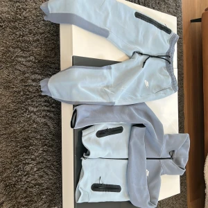 Ljusblå hoodie och byxor från Nike - Säljer en ljusblå hoodie och matchande byxor från Nike. Setet har svarta dragkedjor och detaljer, samt en justerbar huva. Det står XS men är egentligen typ storlek S Perfekt för en avslappnad stil. 🌀priset kan diskuteras.