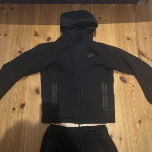 Nike tech nya modellen  - Säljer ett par svarta mjukisbyxor från Nike med smal passform och ribbade muddar vid benslut. Byxorna har snörning i midjan och praktiska dragkedjefickor på sidorna. Materialet är mjukt och bekvämt, perfekt för chill eller träning.