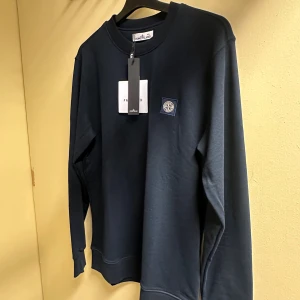 Mörkblå sweatshirt från Stone Island - Snygg mörkblå sweatshirt från Stone Island med klassisk rund hals och lång ärm. Tröjan har en stilren patch med logga på bröstet och är gjord i mjuk bomull. Perfekt för dig som gillar enkel och clean streetwear. Storlek: S,M,L,XL,XXL. Skriv önskad storlek efter lagd order. 