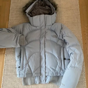 Ljusblå dunjacka från The North Face S - Säljer en snygg ljusblå dunjacka från The North Face med luva. Jackan har ribbade muddar, dragkedja och knäppning framtill samt två fickor. Kort passform. Perfekt för kalla dagar.