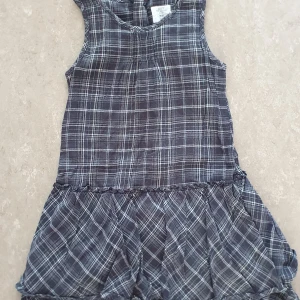 Klänning - Snygg grå ärmlös klänning från H&M med vitt rutmönster och volang nertill. Klänningen har en avslappnad passform och är tillverkad i mjuk bomull, perfekt för en cool och bekväm stil.