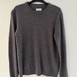 Grå merinoulltröja These Glory Days - Snygg grå stickad tröja från These Glory Days i mjuk merinoull. Klassisk rund hals och långärmad modell med ribbade muddar. Perfekt för dig som gillar stilrena och enkla plagg med skön passform. Storlek M men sitter mer som S