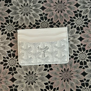 Vit plånbok med mönster - Vit plånbok med ikoniskt grafiskt mönster och flera kortfack. Slimmad och stilren design med tryckt logotyp på framsidan. Perfekt för dig som vill ha något exklusivt och snyggt i fickan.