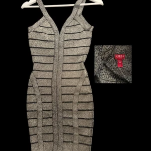 Glittrig silverklänning från Guess - Supersnygg glittrig silverklänning från Guess med smala axelband och v-ringning. Klänningen är kort och har ett tight passform med svarta ränder som ger en cool effekt. Perfekt för dig som vill sticka ut och glänsa.