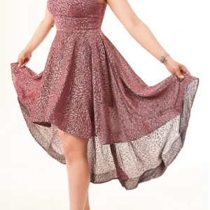 Glittrig vinröd klänning med mönster - Supersnygg vinröd klänning med glittrigt mönster och asymmetrisk fåll. Ärmlös design och markerad midja ger en riktigt fin siluett. Perfekt för dig som vill sticka ut med en unik look. Tyget har en lätt glans och struktur.